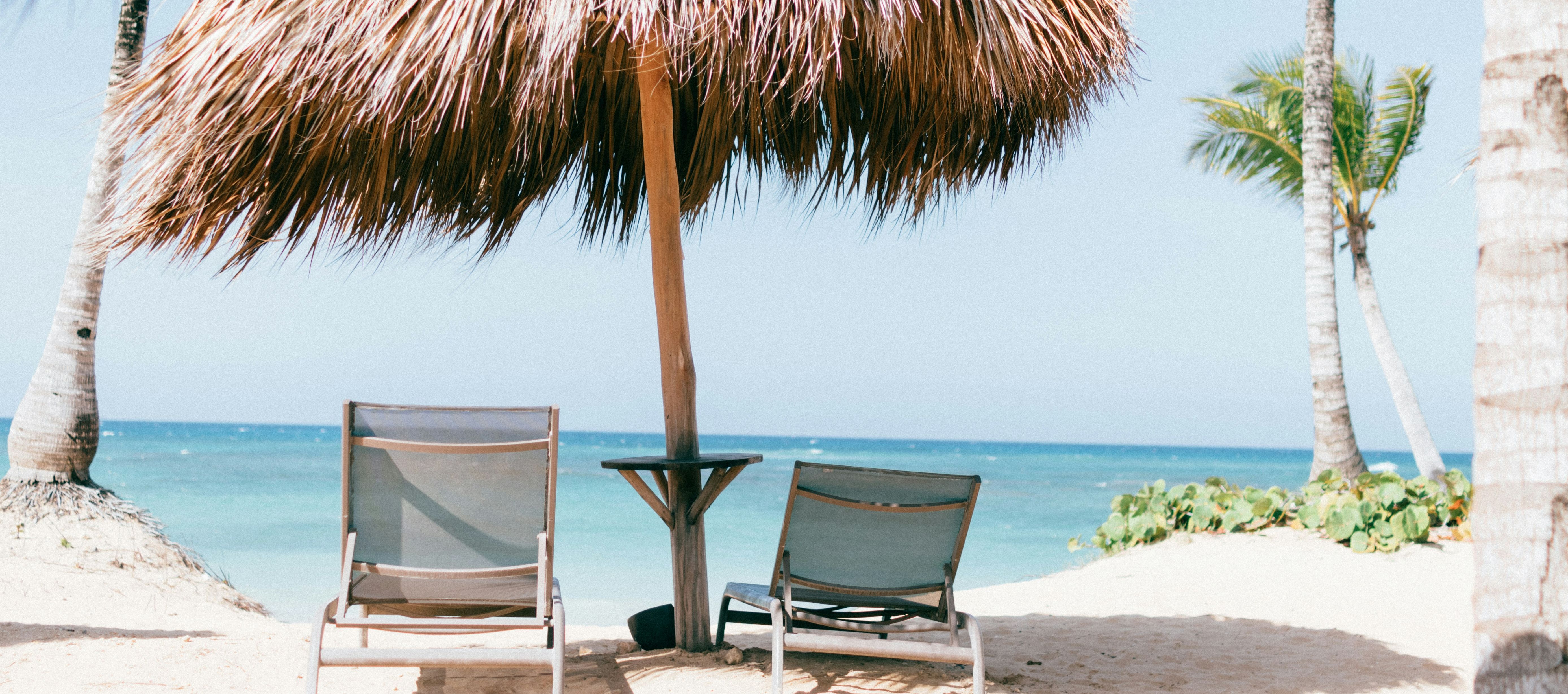 Ein Bild am Strand mit zwei Liegestühlen und einem Sonnenschirm. 